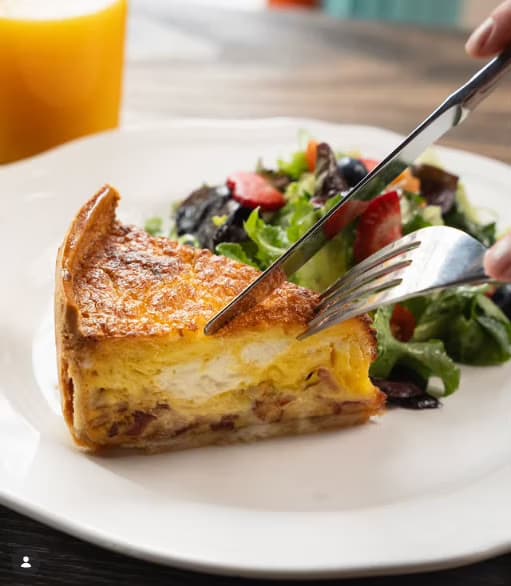 A slice of golden quiche Lorraine beside a fresh salad